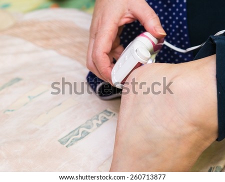 Picture of woman removing dry skin from her foot with grinder