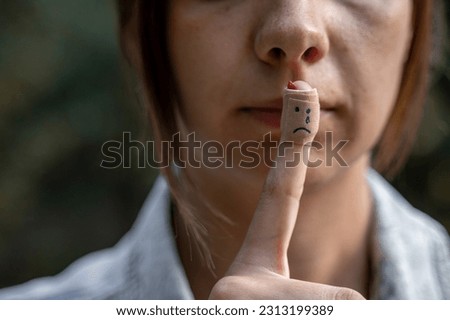 Picture of women trying to hide her pain and depression. Depressed woman holding her injured finger above lips. Finger has adhesive bandage over finger with sad smiley on it. Patch injuries.  