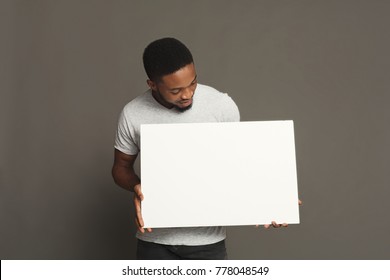Picture of young african-american man holding white blank board on grey background, copy space