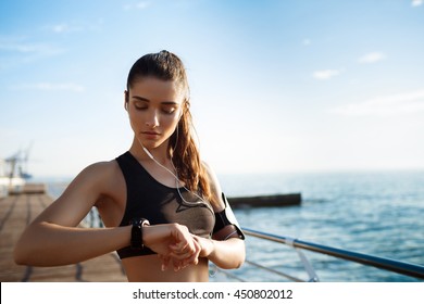 Picture Of Young Attractive Fitness Girl Looking At Watch With Sea Coast On Background