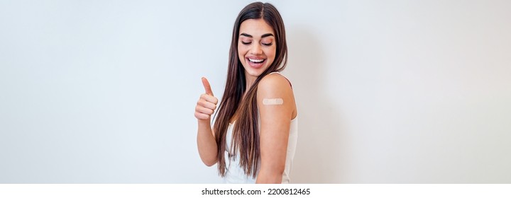 Picture Of Young Brunette Woman, In White Background, Giving Thumbs Up, Looking At Shoulder With Band Aid.