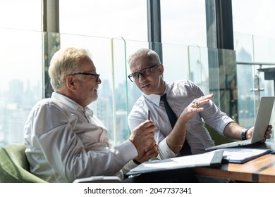 Picture Of Young Business Man Taking To His Older Business Partner. They Are In White Shirt And Black Tie. They Are In A Hotel Lobby. 