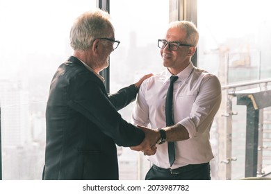 Picture Of Young Business Man Talking To His Older Business Partner. They Are In White Shirt And Black Tie. They Are Sitting On A Table In A Hotel Lobby. 