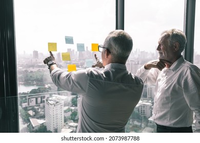 Picture Of Young Business Man Talking To His Older Business Partner. They Are In White Shirt And Black Tie. They Are Sitting On A Table In A Hotel Lobby. 