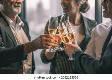 Picture Of Young Business Man And Woman Talking To His Older Business Partner. They Are In White Shirt And Black Tie. They Are Sitting On A Table In A Hotel Lobby. They Are Holding A Champagne Glass. 