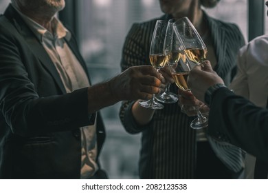 Picture Of Young Business Man And Woman Talking To His Older Business Partner. They Are In White Shirt And Black Tie. They Are Sitting On A Table In A Hotel Lobby. They Are Holding A Champagne Glass. 