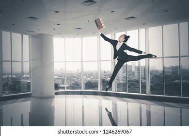 Picture of young businesswoman reading a book and jumping near the window. Shot in the office - Powered by Shutterstock