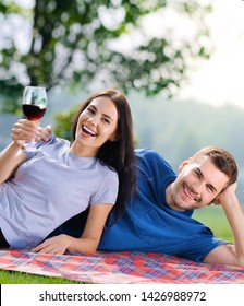 Picture of young couple in love, lying together on a picnic blanket with wine, outdoors