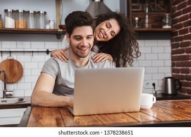 Picture Of Young Couple Man And Woman 30s Looking At Laptop On Table While Having Breakfast In Kitchen At Home