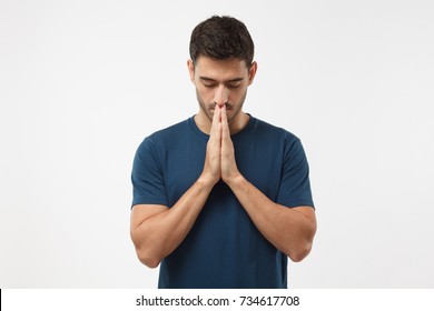 Picture of young guy dressed casually isolated on grey background, having put hands together in prayer or meditation, looking relaxed and calm, dreaming and waiting for all best