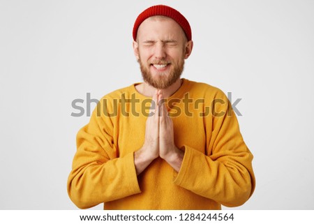 Picture of young guy dressed casually isolated on white background, having put hands together in prayer, looking concentrated with closed eyes, wishing dreaming and waiting for all best