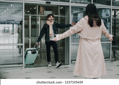 Picture of young man comes out of airport and wants to hug woman that goes to him. Sweet meeting after lonely days of business trip or travel. Happy to see each other. Excited and amazed
