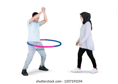 Picture Of A Young Man And His Wife Exercising With A Hula Hoop In The Studio, Isolated On White Background