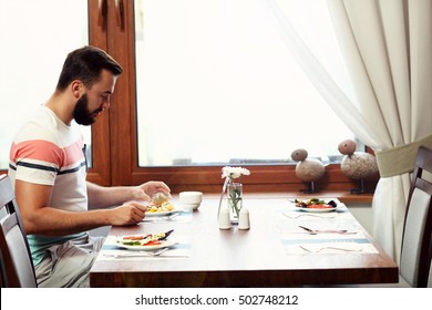 Picture Of Young Man Sitting Alone At Hotel Restaurant Table And Eating Breakfast