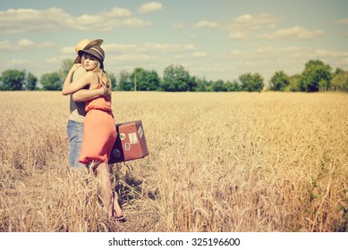 Picture Of Young Man And Woman Hugging In Summer Countryside. Romantic Couple Standing With Old Suitcase On Vintage Toned Countryside Background.