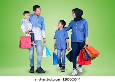 Picture Of Young Muslim Family Holding Shopping Bags While Walking Together In The Studio With Green Screen