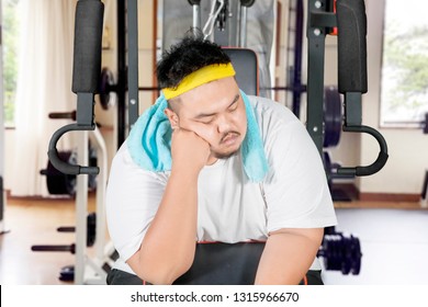 Picture Of Young Obese Man Looks Lazy While Sleeping On The Exercise Machine. Shot In The Gym Center