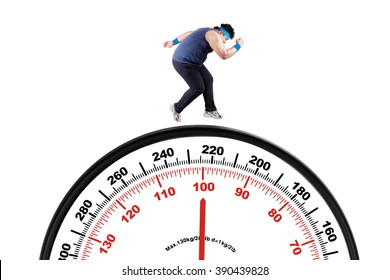 Picture of a young overweight person wearing sportswear and running above a big scale, isolated on white background