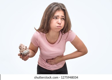 Picture Of Young Woman Hold Eclair. She Is Going To Puke. Model Hold Hand On Stomach. She Feels Bad. Isolated On White Background.