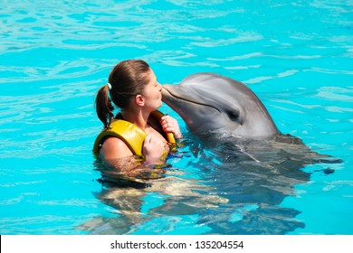 A picture of a young woman kissing a dolphin in a turquise water