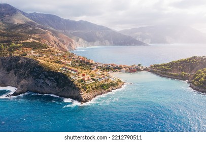 Picturesque aerial shot of colorful fishing Asos village houses on Cephalonia island, Greece. Steep cliff banks washed by blue Ionian Sea waves.