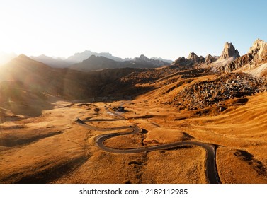 Picturesque aerial view on winding road in autumn mountain valley at sunset. The golden sunset light illuminates the mountains and orange grass. Passo Giau, Dolomite Alps, Dolomites, Italy