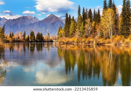 Picturesque autumn landscape with reflection of mountains and yellowed forest in calm blue water. Baikal region, Buryatia, Tunka foothill valley, Irkut river