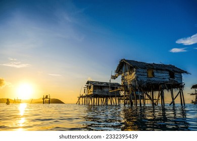 A picturesque Bajau stilt houses gracefully perched above the glistening water enhanced by the breathtaking backdrop of a radiant sunrise or sunset.