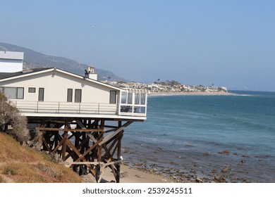 A picturesque beach house perched on a cliff overlooking the ocean. The serene setting features expansive water views and a tranquil atmosphere, ideal for relaxation and coastal living. - Powered by Shutterstock