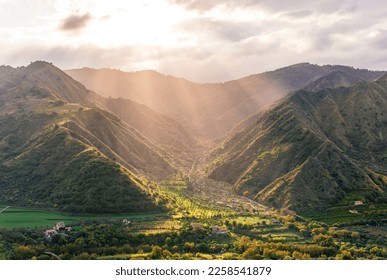 picturesque canyon between two mountain tops with green slopes , illuminated with golden sunset or sunrise rays and nice town below