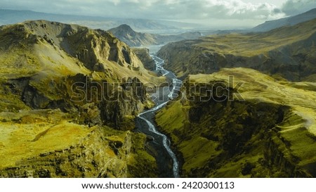 The picturesque canyon and river along a famous Laugavegur hiking trail. Amazing Icelandic landscape of volcanic mountains and river in cloudy weather with green grass and moss. Iceland in august