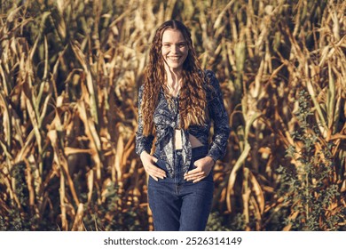 In a picturesque cornfield, a joyful young woman stands confidently in a striking pose, her bright smile radiating warmth under the golden glow of the sunlight, surrounded by tall, lush cornstalks - Powered by Shutterstock