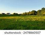 A picturesque countryside scene with green fields, houses in the distance, and trees bathed in the warm light of the setting sun, showcasing the tranquility and beauty of rural life