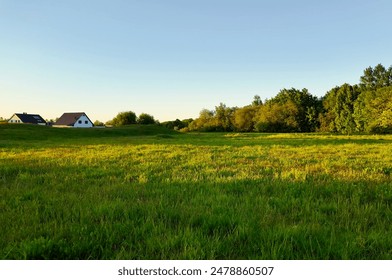 A picturesque countryside scene with green fields, houses in the distance, and trees bathed in the warm light of the setting sun, showcasing the tranquility and beauty of rural life - Powered by Shutterstock