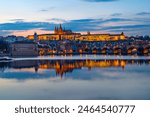 A picturesque evening view of the Prague additions - the Charles Bridge over the Vltava River and the illuminated Prague Castle with the Goitic Cathedral.