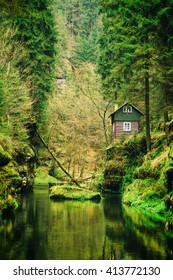 The Picturesque House Surrounded By A Forest Dark Forest In The Gorge Depth Rises Above The Quiet Water Of Forest River. The Cottage Among Spring Forest In The Gorges Of The Czech Switzerland. Colored