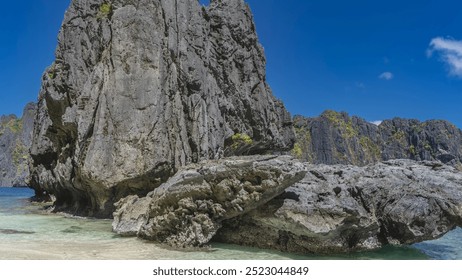 Picturesque karst rocks and boulders on the beach. Steep, furrowed slopes, bizarre outlines. Aquamarine ocean, sandy beach, blue sky with clouds. Philippines. Palawan. Bacuit bay
 - Powered by Shutterstock