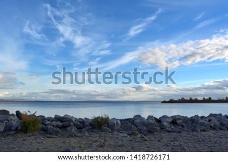 Picturesque landscape with blue river and grey stones on the bank. Beautiful sky panorama with clouds.
