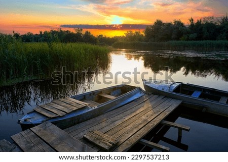 Picturesque landscape with an old rustic wooden pier and old boats at sunset among the reed thickets in the Dnieper Delta. Estuaries of the Dnieper River, Konka River, Kherson region, Ukraine