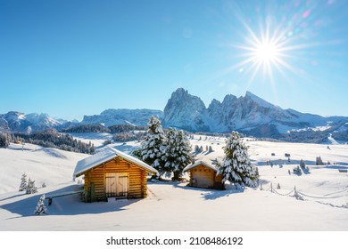 Picturesque landscape with small wooden log cabin on meadow Alpe di Siusi on winter time. Seiser Alm, Dolomites, Italy. Snowy hills with orange larch and Sassolungo and Langkofel mountains group