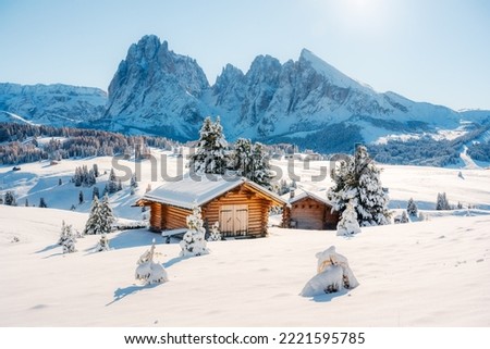 Picturesque landscape with small wooden log cabin on meadow Alpe di Siusi on sunrise time. Seiser Alm, Dolomites, Italy. Snowy hills with orange larch and Sassolungo and Langkofel mountains group
