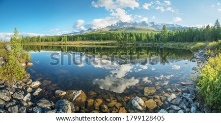 Picturesque mountain lake in the summer morning, Altai. Beautiful reflection of mountains, sky and white clouds. Clear water, stones at the bottom.