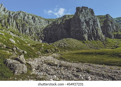 Picturesque mountain landscape with green alpine grasslands, dry riverbed and steep rocky cliffs in the vast Malaiesti Valley in Bucegi mountains, Romania. Romanian travel destinations.