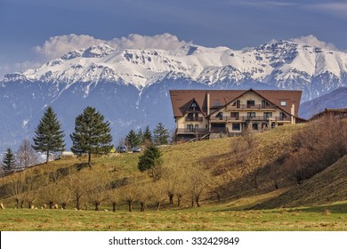 Picturesque mountain landscape with modern chalet and snowy Bucegi mountains in spring, Romania. Scenic touristic vacation destinations.