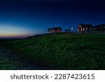 Picturesque night landscape with French houses and huts with luminous windows. Located on a hill with green grass on the ocean, in the English Channel.