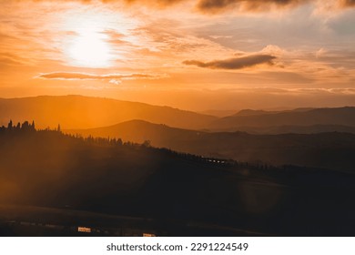 The picturesque rolling hills of Tuscany are captured during a breathtaking sunset, with the sun's warm glow casting a golden light across the landscape. Vineyards and olive groves dot the hillsides. - Powered by Shutterstock