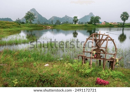 A picturesque scene of a bamboo structure of Devi Druga  sitting in the middle of a lush green field, surrounded by a serene lake. In the background, majestic mountains rise up. 