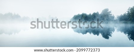 Picturesque scenery of the forest lake in a thick white fog. Reflections on the water. Dark atmospheric landscape. Fall season. Nature, ecology, environmental conservation, eco tourism