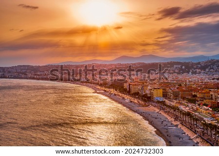 Picturesque scenic view of Nice, France on sunset. Mediterranean Sea waves surging on the beach, people are relaxing on the beach, cars driving the road. Nice, France