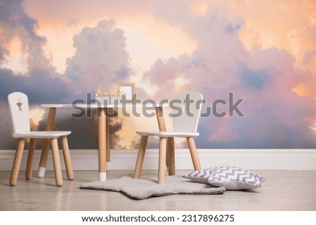 Picturesque sky with clouds as wallpaper pattern. Baby room interior with table and chairs near wall